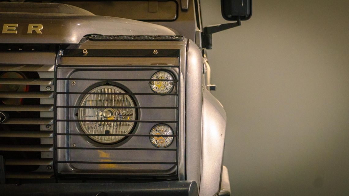 Detailfoto van de koplamp en knipperlicht van een grijze 8 cilinder Landrover Defender